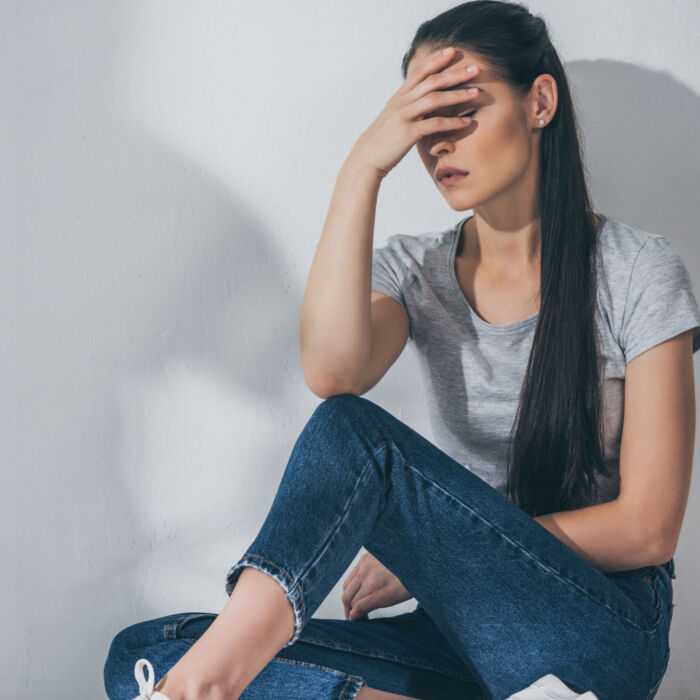 full length view of depressive brunette girl sitting with hand o